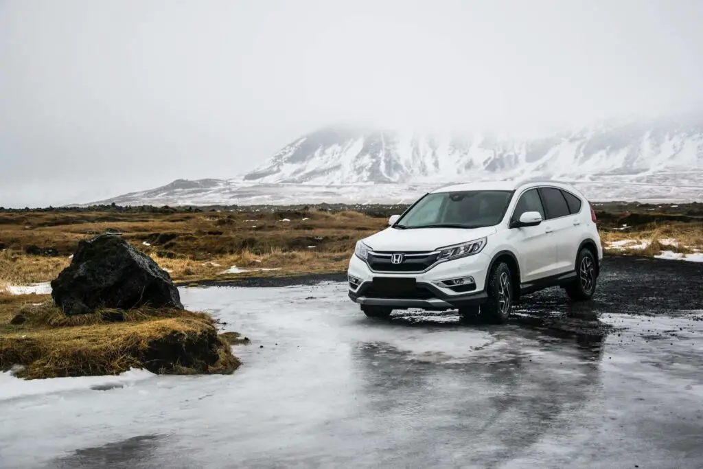 White Honda SUV  next to a frozen lake, mountains in the distance